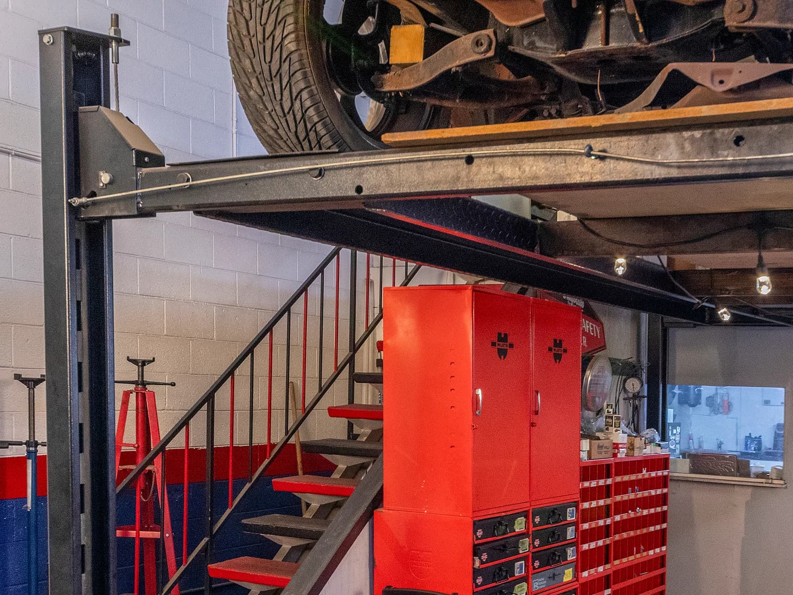 Underside of a vehicle raised on a lift above red tool cabinets