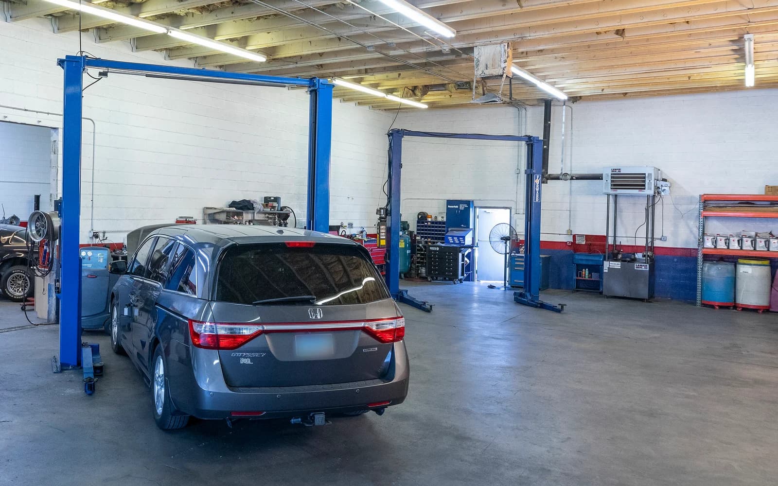 Grey minivan in a service bay beside a two-post lift